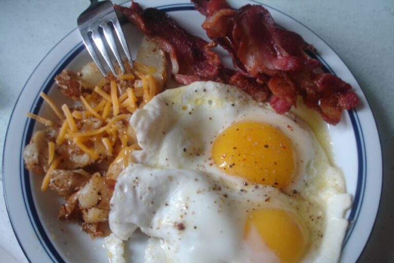 High-cholesterol eggs sunny side up, bacon, and home fries with cheddar cheese