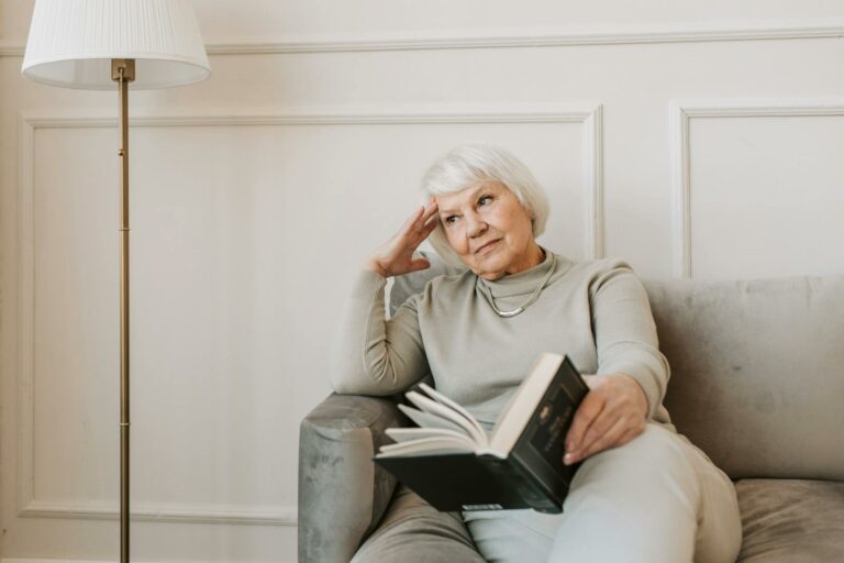 Pensive Alzheimer's Caregiver Sitting on Gray Couch with a Book